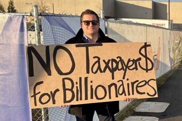 No tax protesters holding a sign opposing billionaire tax policies.
